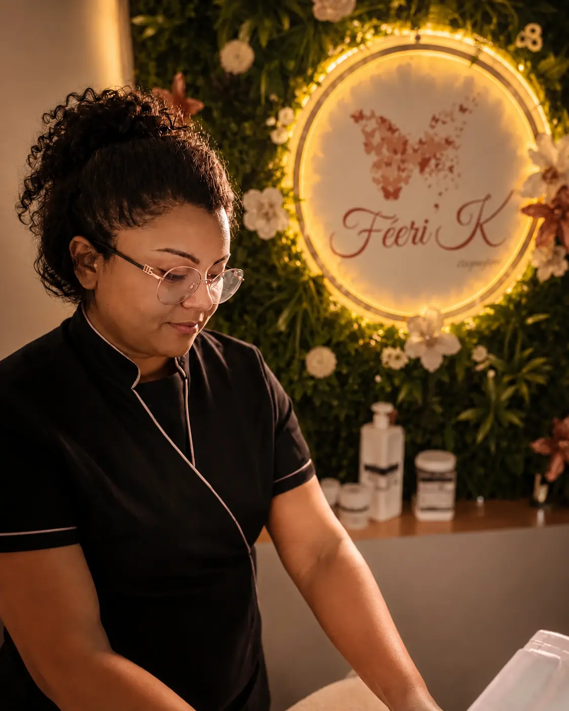 Ericka, esthéticienne, au travail dans l'institut Féeri'K devant le mur végétal et l'enseigne lumineuse